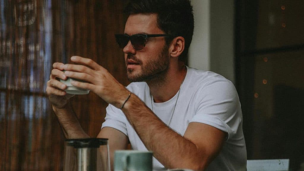 A man wearing sunglasses holding a cup while sitting at a table.