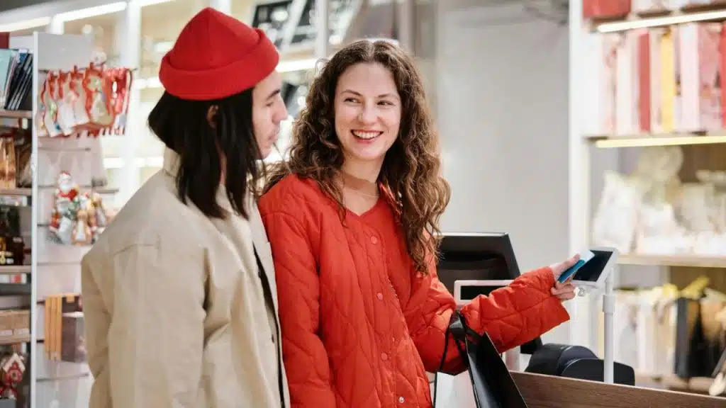 A woman smiles while making a contactless payment at a store counter.