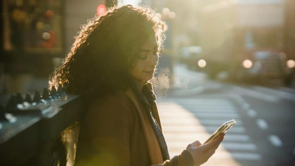 A woman standing outdoors and looking at her phone.