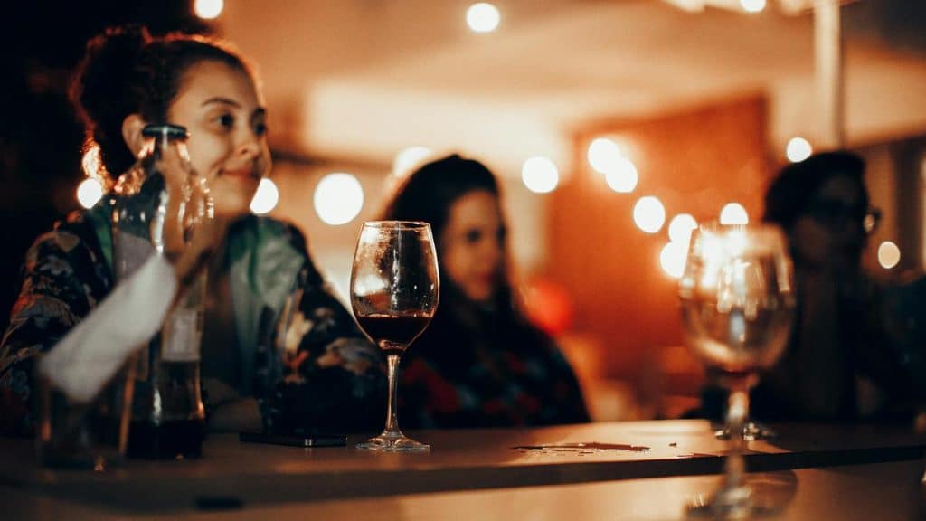 A woman sitting at a bar with drinks and warm lights in the background.