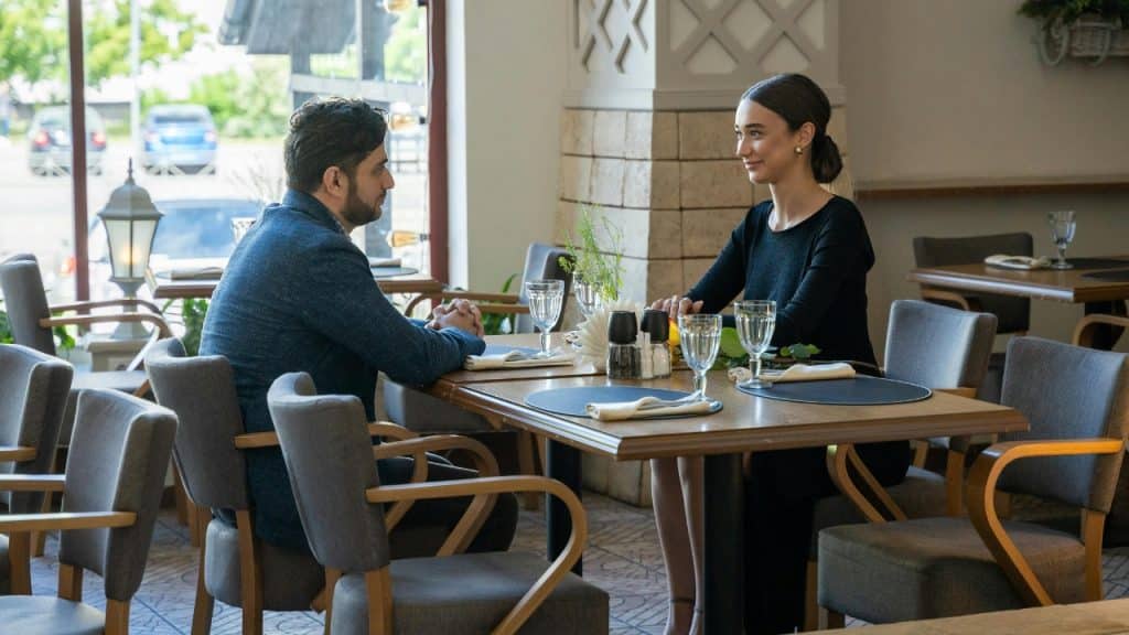 A man and woman sit across from each other at a restaurant table with glasses.