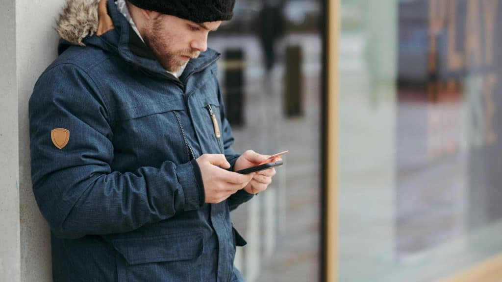 A man in a winter jacket using his phone outdoors.