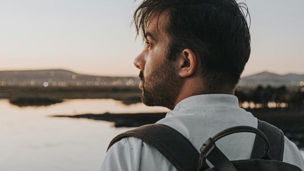 A man with a backpack looking out over a lake at sunset.