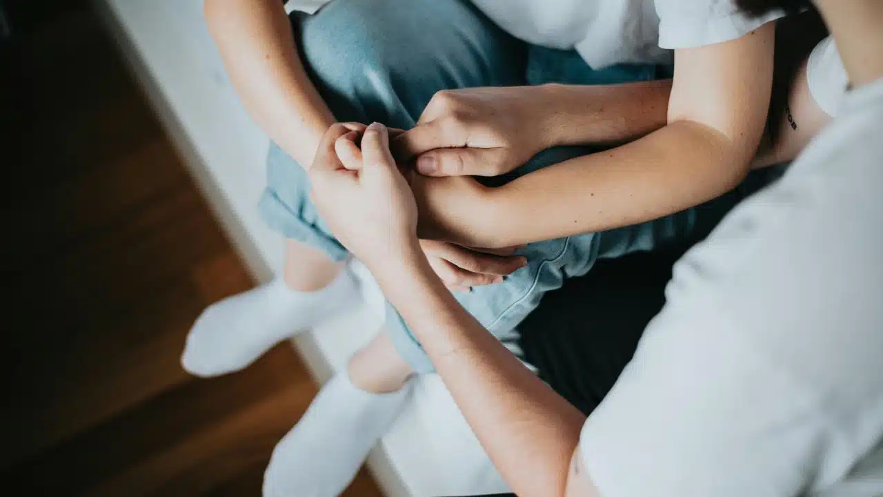 A person holds another’s hand in comfort.