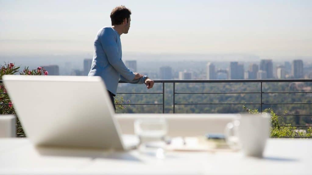 A man leaning on a balcony railing and looking over a city skyline.