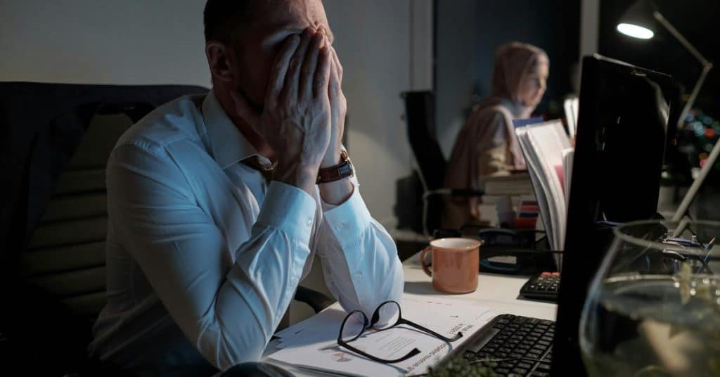 A tired man covering his face while working late at an office desk.