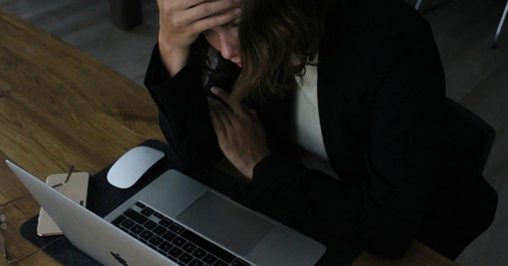 A stressed person holding their head while working on a laptop.