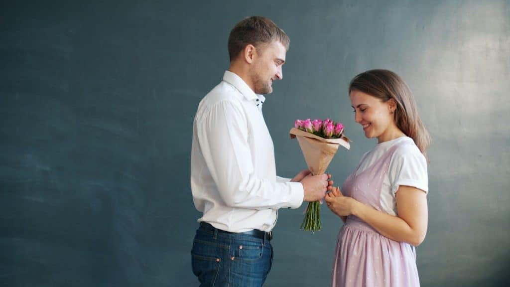 A man gives a woman flowers in front of a dark background.