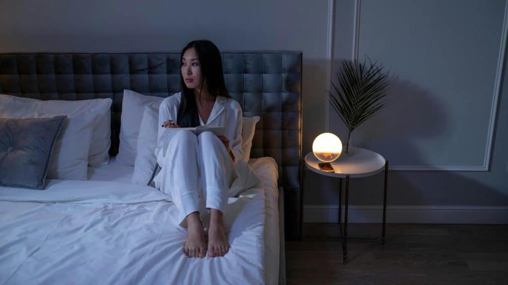 A woman sitting on a bed at night, writing in a notebook.
