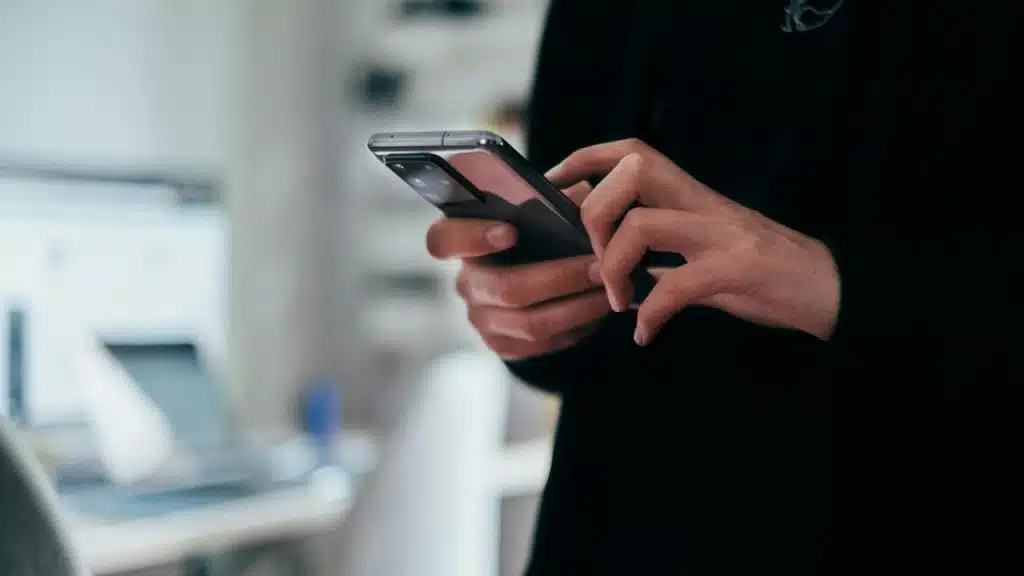 A person using a smartphone with both hands indoors.