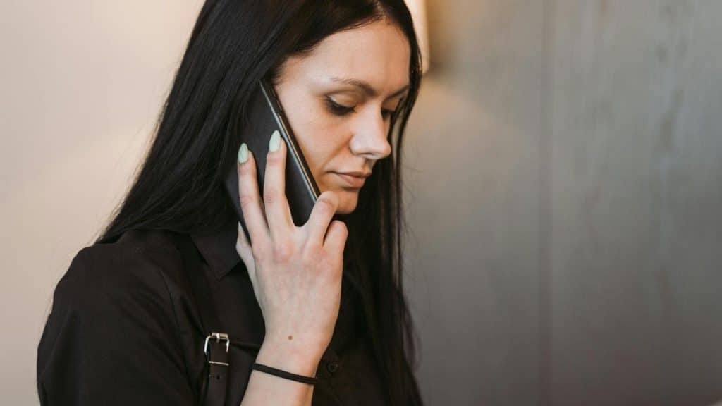 A woman with long dark hair talks on a phone, looking down.