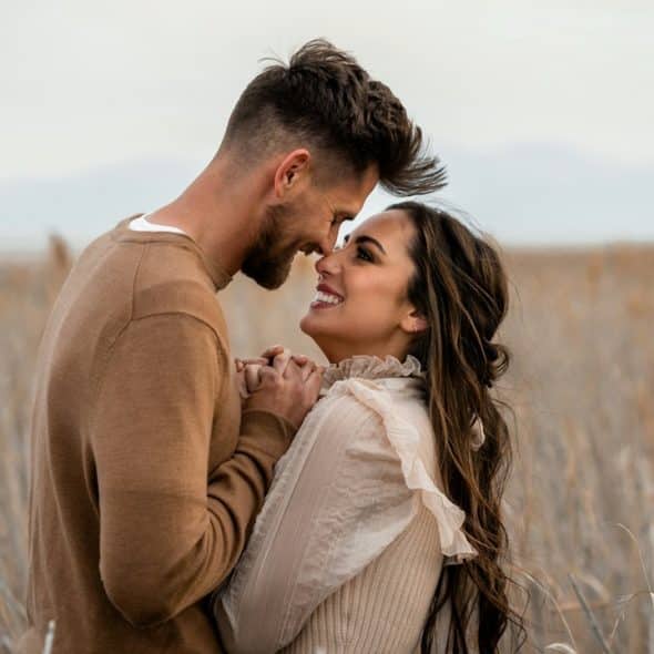 Couple looks at each other lovingly in a field.