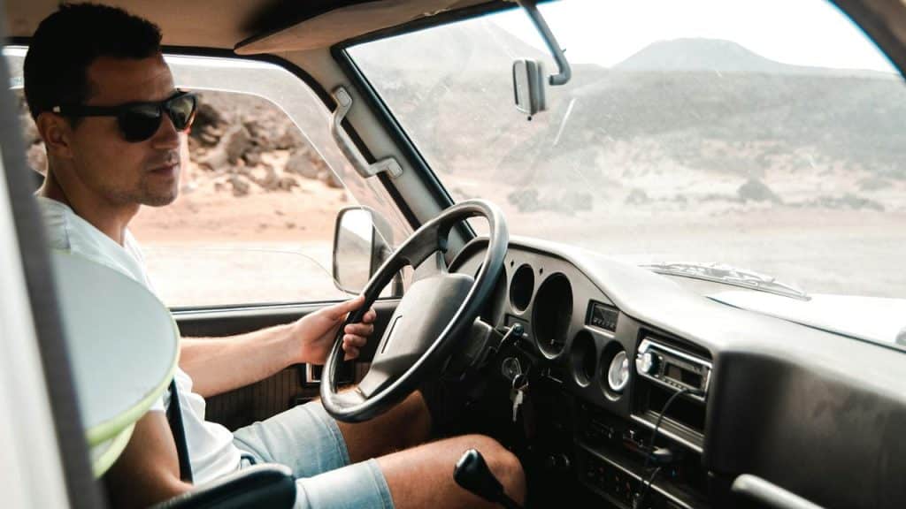 A man wearing sunglasses driving a vehicle through a desert landscape.