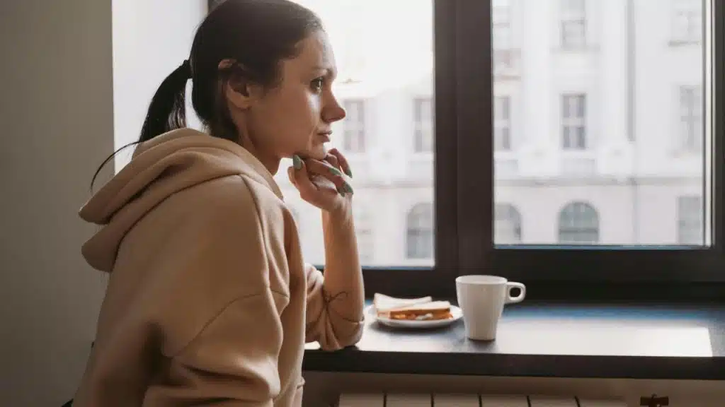 A woman in a hoodie gazes out a window