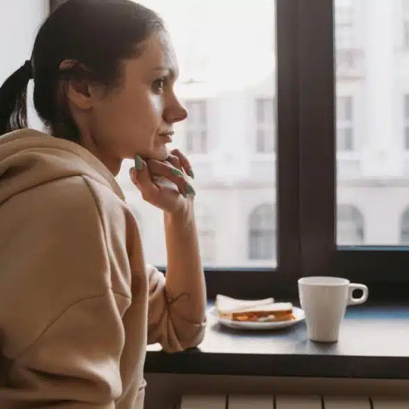 A woman in a hoodie gazes out a window