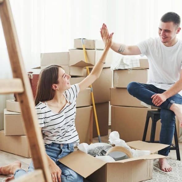 A couple sitting among moving boxes and giving each other a high-five in their new home.