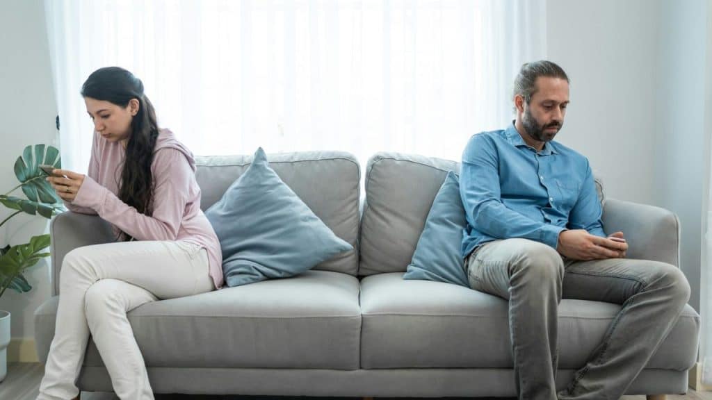 A man and woman sit on opposite ends of a sofa looking at their phones.