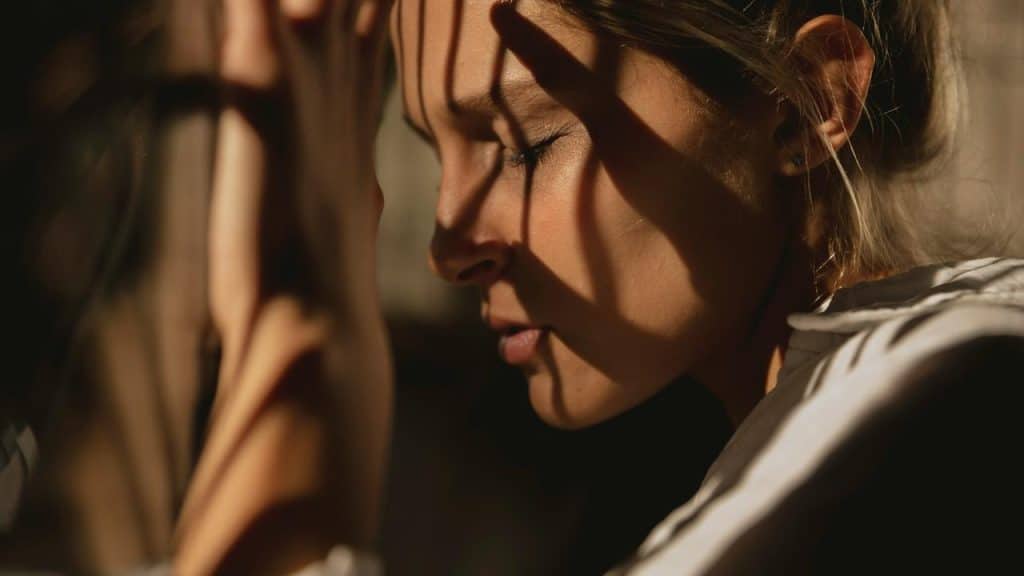 A woman with eyes closed, holding her head in a stressed or contemplative pose.