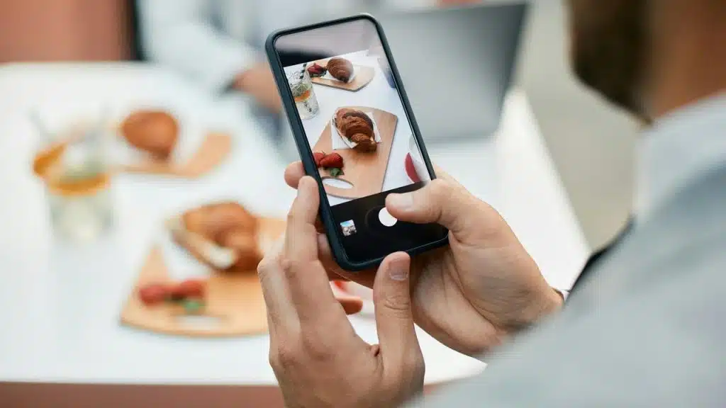 A person taking a photo of a croissant and strawberries with a smartphone.
