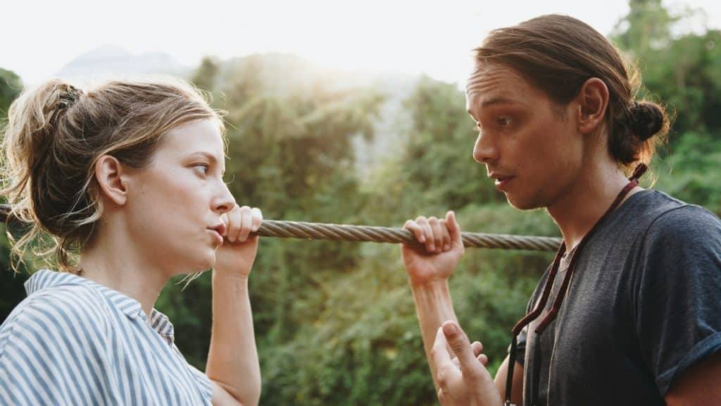 A man and woman talking while holding onto a thick rope bridge in a forest.