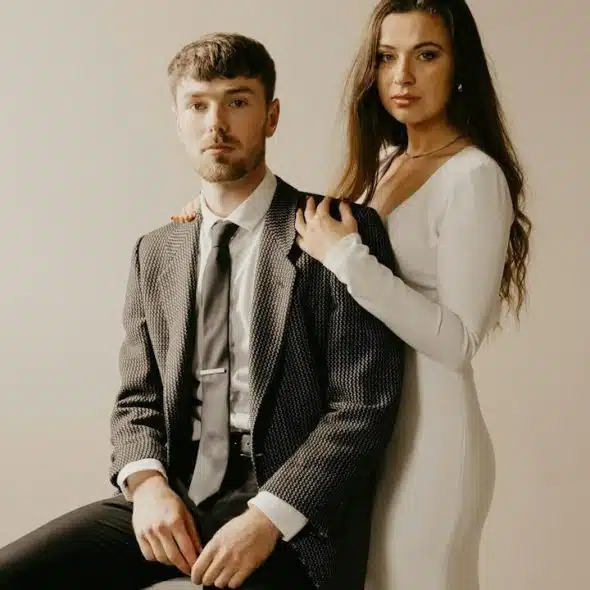 A woman resting her hands on a sitting man’s shoulders while she stands behind him.
