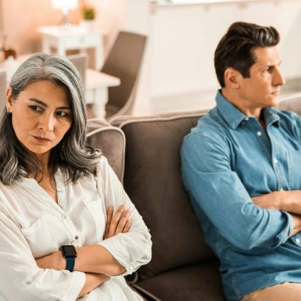 A man and woman sit on a couch with arms crossed, facing away from each other.