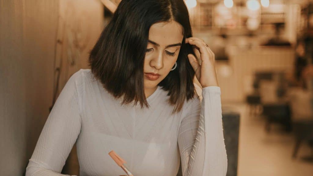A woman writing thoughtfully at a table in a softly lit cafe.