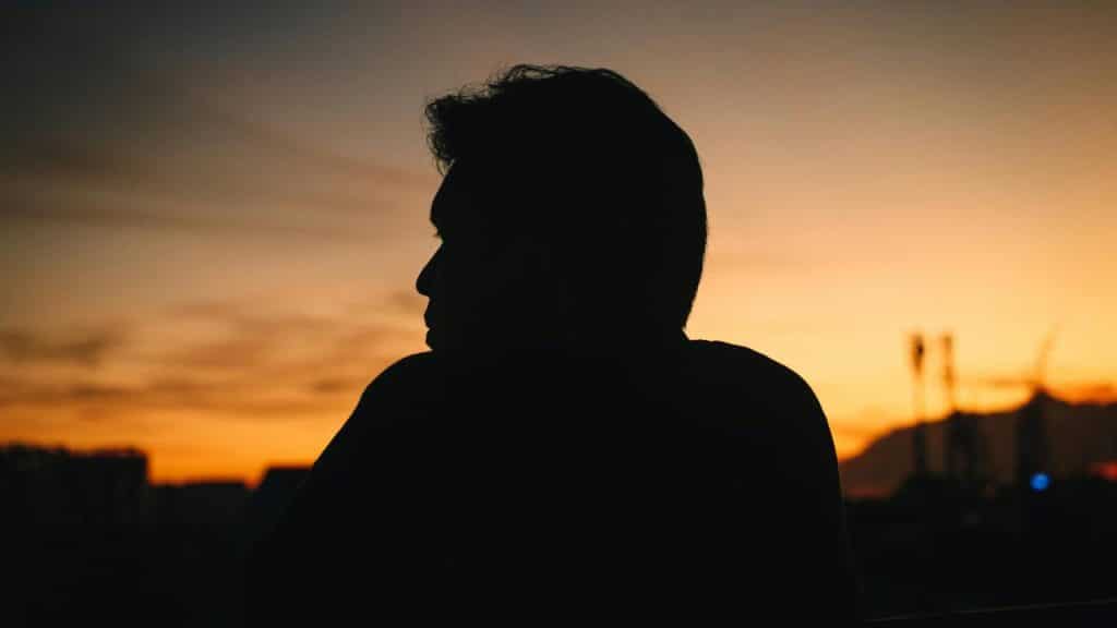 A silhouette of a man against a sunset sky over a city.