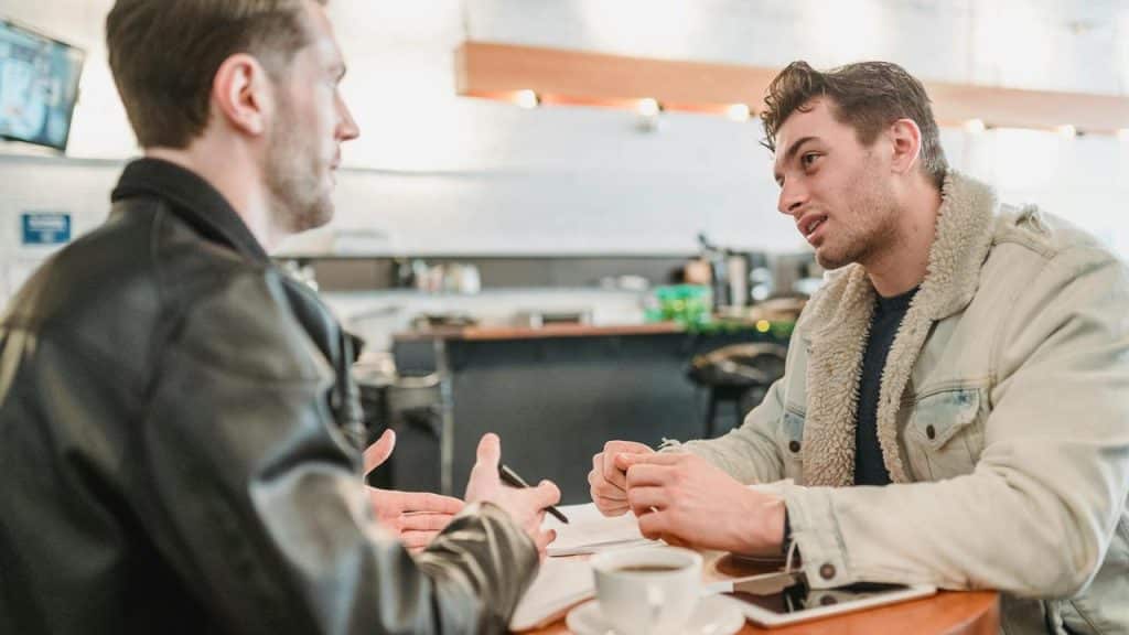 A pair of men talking across a table with coffee in a café.