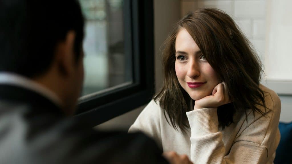 A woman rests her chin on her hand while looking at an unseen person.