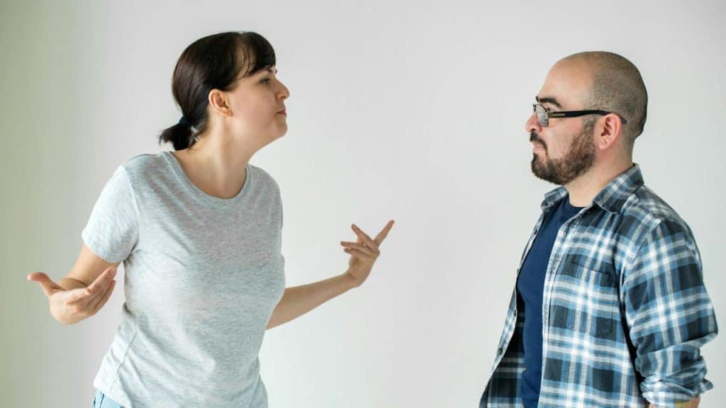 A woman stands gesturing with open hands while facing a man in a plaid shirt.