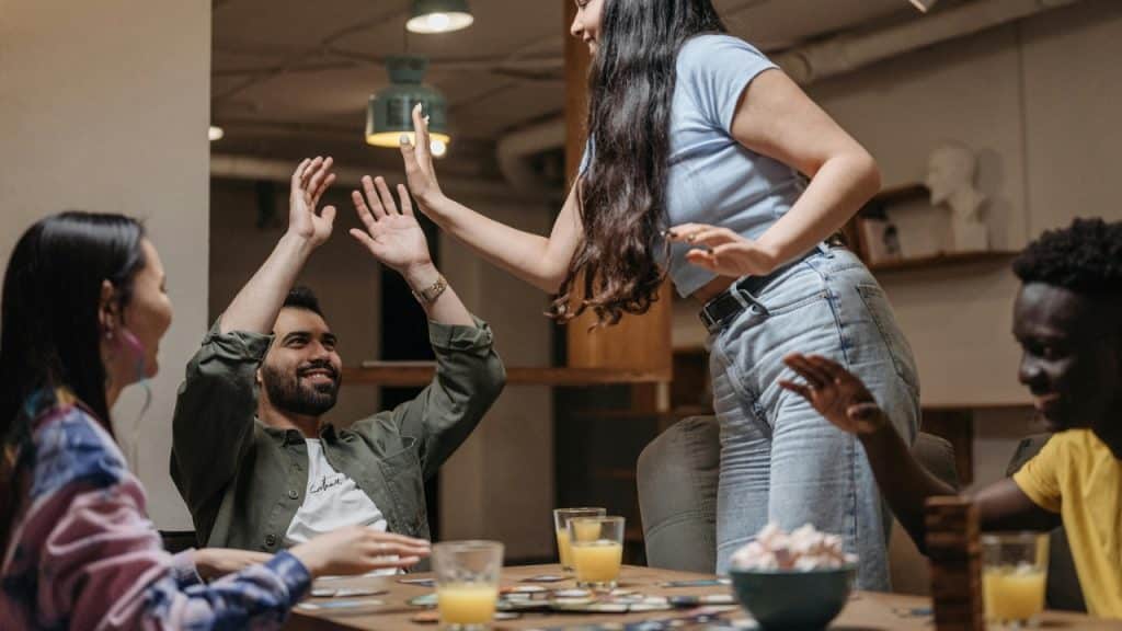 A group of people sitting at a table reach up to high-five each other.