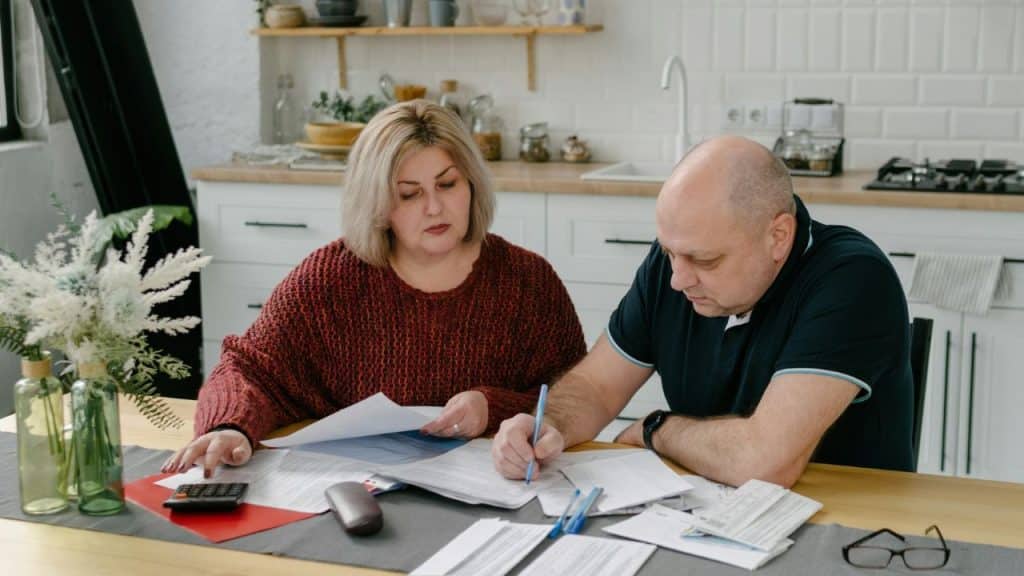 A couple sits at a table reviewing documents and using a calculator together.