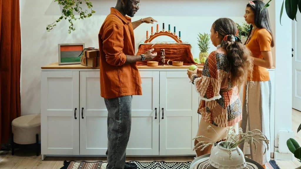 A family standing together while lighting candles on a menorah at home.