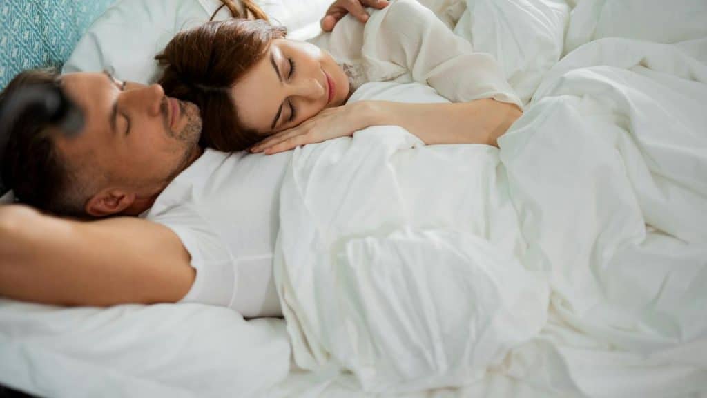 A couple sleeping together comfortably in bed.