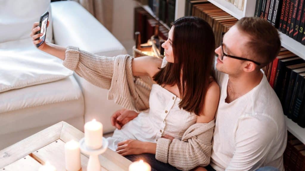 A young couple sits together while taking a selfie with a smartphone.