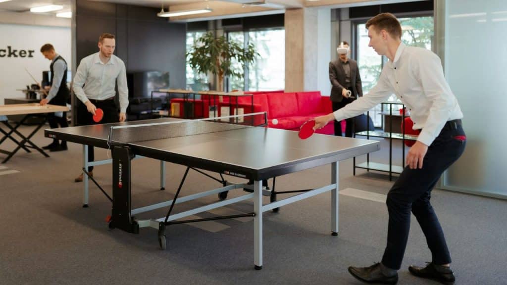 Men in business casual attire play ping-pong in a modern office lounge area.