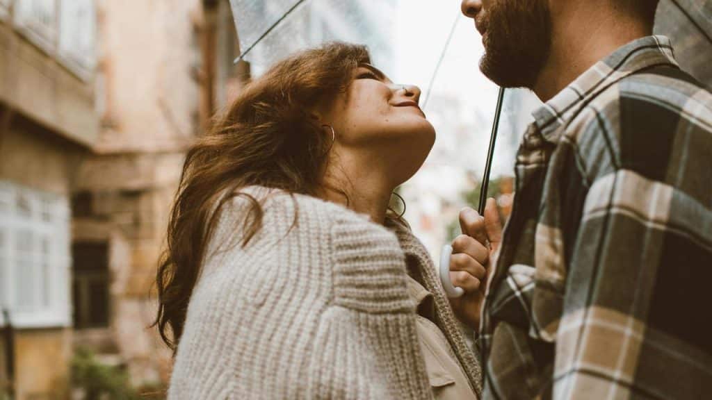 A couple standing close together under an umbrella on a rainy street.