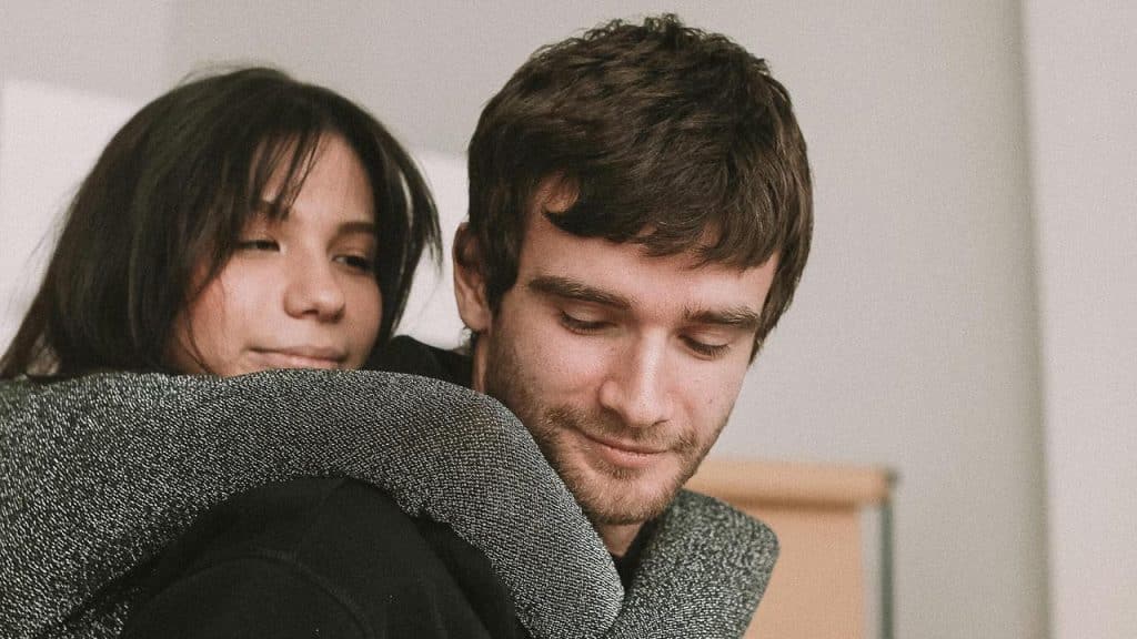 A woman hugging a man from behind as he looks down with a gentle expression.