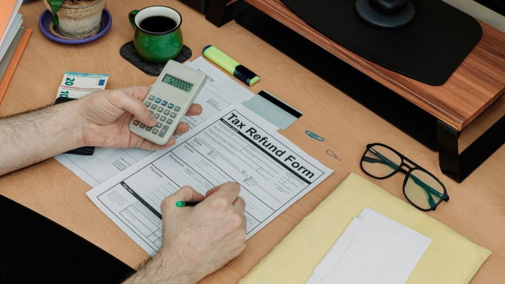 A person uses a calculator while filling out a paper tax refund form at a desk.
