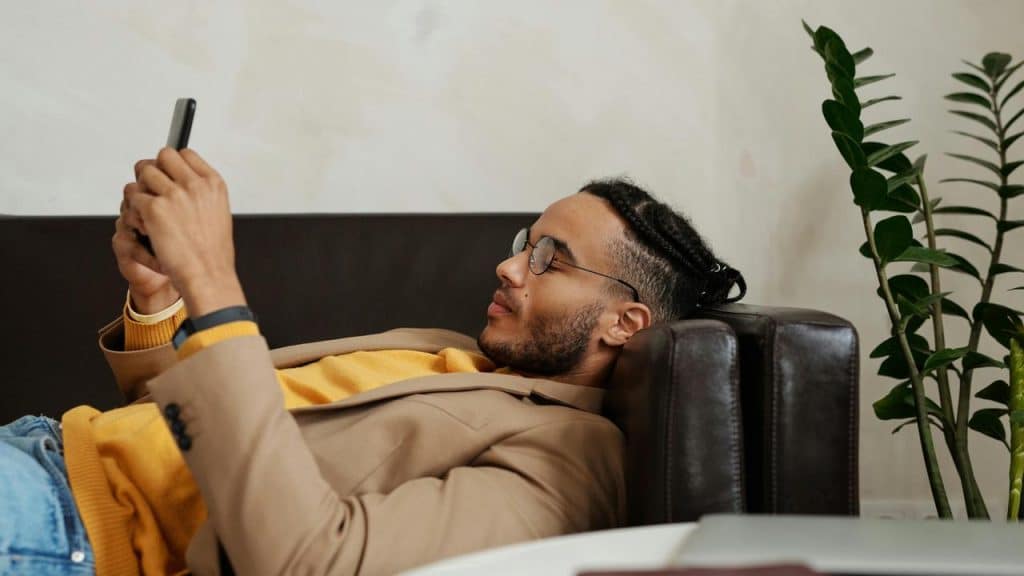 A man lying on a couch using his smartphone indoors.