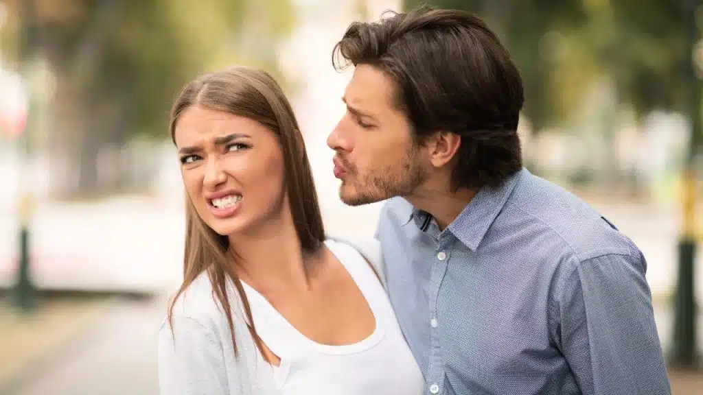 A man leans toward a woman who is recoiling with a disgusted expression.