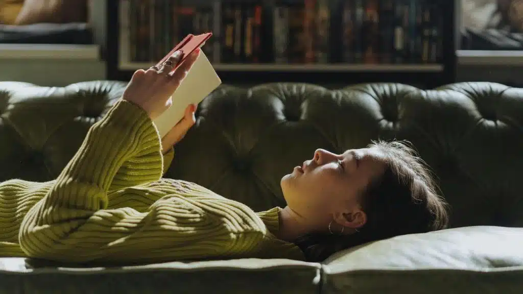 A woman lying on a couch reading a book.