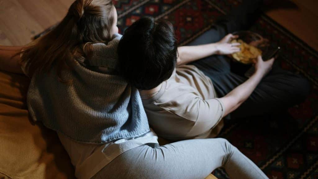 A couple sitting together and sharing a bowl of snacks.