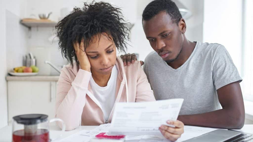 A man and woman sit together looking concerned while reviewing paperwork at a table.