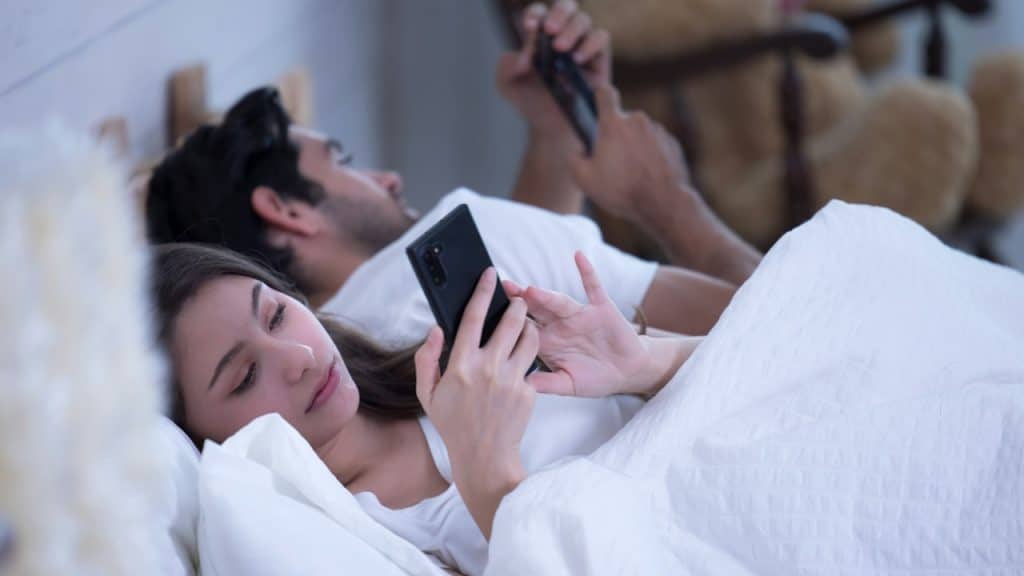 A man and a woman using their cell phones while lying in the bed.