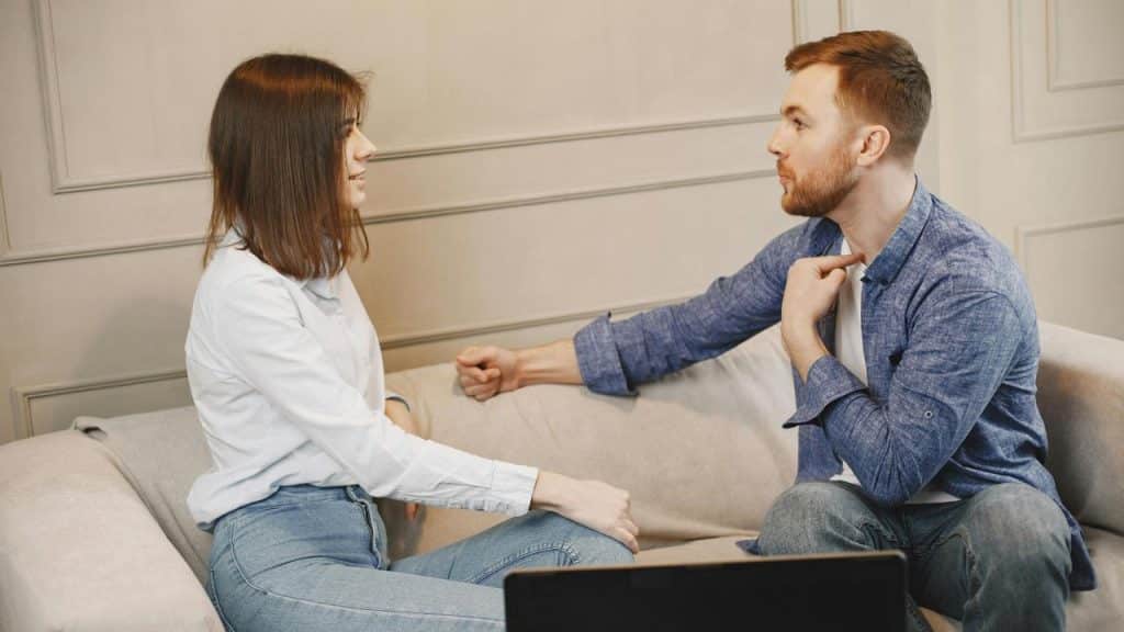 A man and woman talking while sitting on a couch.