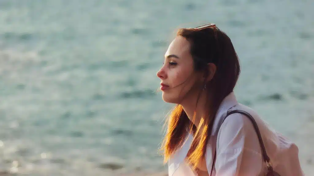 A woman gazes thoughtfully at the sea while sitting near the water.