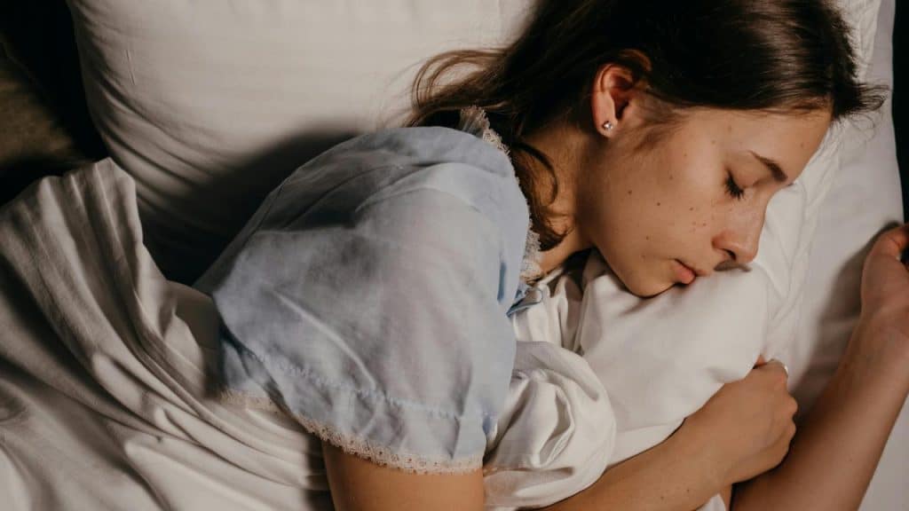 A young woman sleeping peacefully while hugging a pillow in bed.