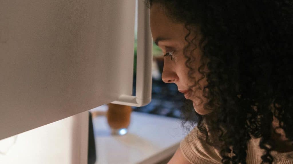 A woman looking at a fridge in a dimly lit room.